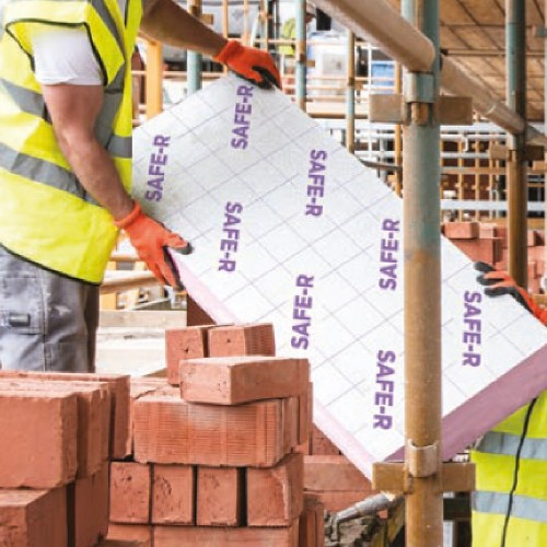 Construction worker carrying a pink phenolic insulation board on site.
