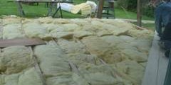 Worker installing insulation between floor joists outdoors