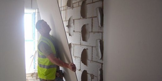 Construction worker installing plasterboard on a block wall